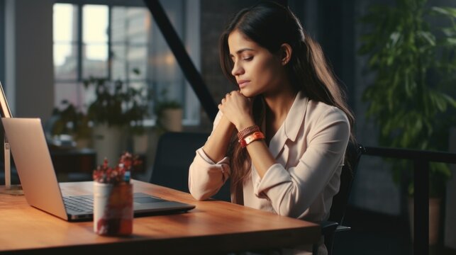 A woman is seen sitting at a table, focused on her laptop. This image can be used to depict working from home, remote work, or technology in modern society
