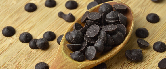 Delicious dark chocolate drops in wooden spoon