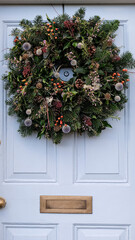 Fototapeta na wymiar Christmas mood: festive elegant charming christmasy themed winter natural wreath on a blue wooden door. Wreath decorated with flowers, fir tree. Christmas wreath on a light grey blue wooden door