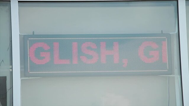 electric digital sign that says we speak english greek italian hindi telugu persian, horizontal rectangle red writing on black background in window