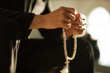 Side view closeup of unrecognizable man holding rosary beads in prayer lit by sunlight, copy space