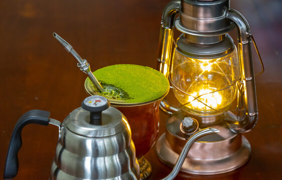 Traditional chimarrão prepared with yerba mate (Ilex paraguariesis) in a porongo gourd, next to a vintage lamp and barista-style gooseneck kettle