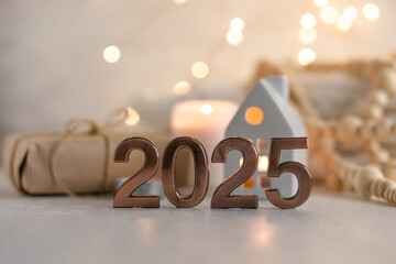 Happy new year 2025 postcard. Golden digits in front of Christmas lights, candles, gift box. White...