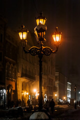 A glowing snow-covered lantern stands in the city on the street in winter in the snow. Photography,...