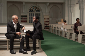 Full length portrait of African American pastor advising senior man after Sunday service in...
