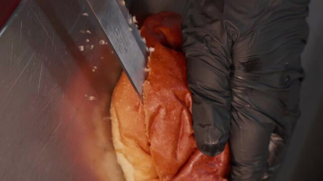 Chef in black gloves making burge. cut the burger bun. Close-up of a skilled craftsman working at the workplace 