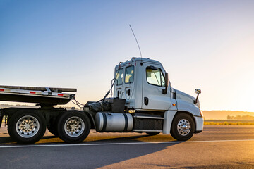Day cab white local carrier big rig semi truck with step deck semi trailer driving on the road...