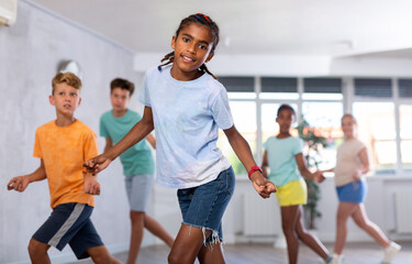 Dynamic little boy training Rock-and-Roll dance poses in dancehall with other attendees of dancing...