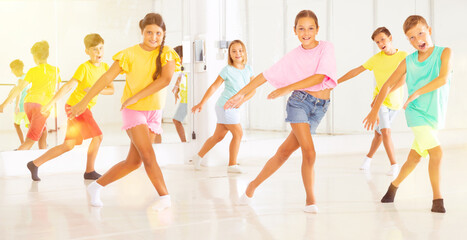 Naklejka premium Group of cheerful tween children learning movements of vigorous dance in choreography lesson.