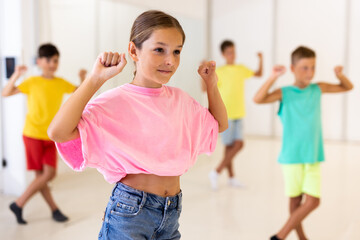 Portrait of cheerful preteen girl learning energetic dance moves with group of children in choreography class .