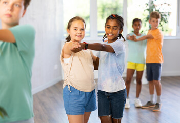 Interested modern tweens, smiling dark-skinned boy and european girl learning to dance waltz as...