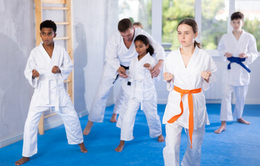 Group of preteen children of different nationalities in kimono trying new martial moves at karate class