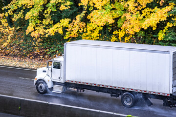 Powerful day cab big rig white semi truck transporting goods in long box trailer driving on the...