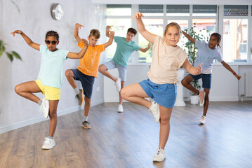 Group of positive juvenile boys and girls engaged in Breakdancing in training room during workout session