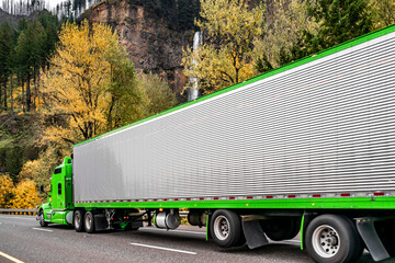 Stylish classic green big rig semi truck tractor carry cargo in shiny refrigerator semi truck...