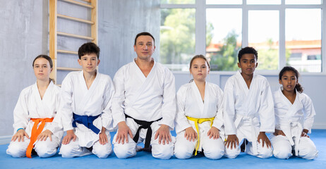 International group of preteen martial arts fighters in white kimonos with experienced coach...
