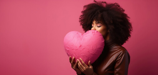 Beautiful afro-american curly woman hugging big pink heart over pink background. Young adult close eyes enjoy holiday. Copy space. Concept of love, female, beauty, valentine's day.