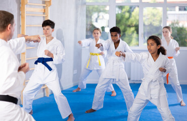 Motivated sporty black girl with group of tweens wearing white kimonos diligently performing kata...