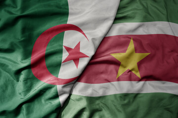 big waving national colorful flag of suriname and national flag of algeria .