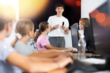 Friendly young teacher standing near an interactive whiteboard telling new material to teenage...