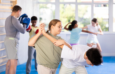 Boy and girl practicing self-defense techniques in group at gym..