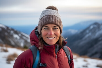 Fototapeta na wymiar Medium shot portrait photography of a pleased woman in her 40s that is wearing thermal wear, snow boots, beanie against mountaintop with a panoramic view of snow-covered peaks background