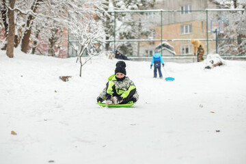 Child girl ride in snow plate. Outdoor play. Cold temperature. Winter time