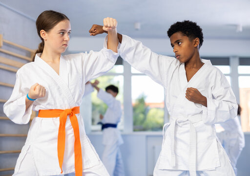 Focused african american teenager in karate uniforms practicing hand strikes and techniques during sparring with girl at martial arts training.. - Powered by Adobe