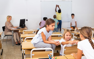 Happy preteen schoolchildren communicating during recess between lessons in classroom