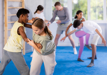 Girls and boys learns to do power grip with trainer during a self-defense lesson in the gym