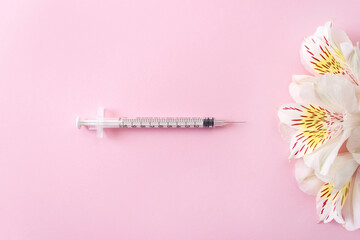 Flowers and medical syringe on pink background. Minimal concept of beauty injections. Selective...