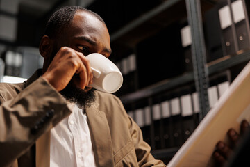Private investigator drinking coffee while examining police documentation. African american man...
