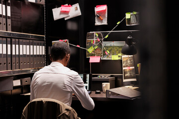 Police investigator working overtime analyzing evidence to solve crime. Criminalist sitting at...