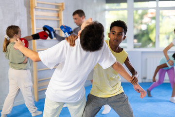 Fototapeta na wymiar Two boys practicing self-defense techniques in group at gym..