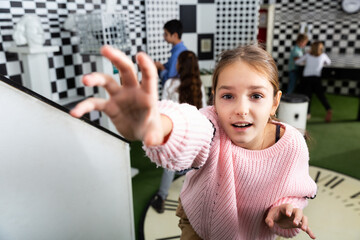 Tween girl trying very hard to reach out key subject of puzzle in chess quest room, holding out her...
