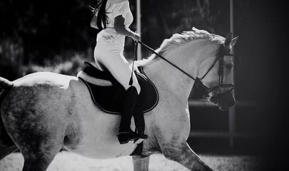 Rolgordijnen A black and white image of a rider riding a white horse at an equestrian competition. Equestrian sports and horse riding. The horse gallops. Jumping competition. ©  Valeri Vatel