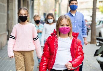 Focused preteen girl in pink protective mask walking along city street on spring day. New life...