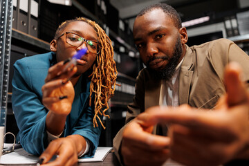 African american man and woman detectives brainstorming and looking at camera. Police investigators partners searching insight for solving crime together in office at night time