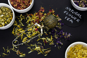 Tea infuser on black background, dried flowers in bowls