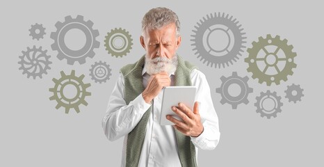 Thoughtful mature man with tablet and drawn gears on grey background