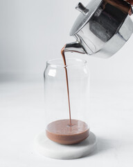 Pouring chocolate milk into can shaped glass on a marble tray, chocolate shake being poured into...