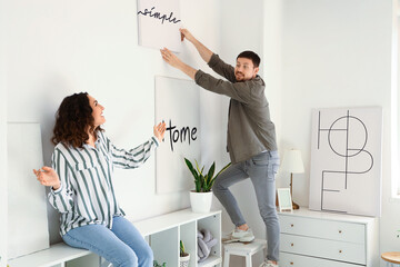 Young couple hanging poster on light wall at home