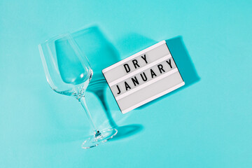 Text Dry January on the decorative lightbox and empty wine glass isolated on blue background - obrazy, fototapety, plakaty