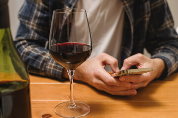 Close-up shot of a man with a glass of wine and holding a phone to track amount of alcohol or to a wine in an app.