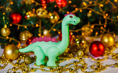 Green dragon on Christmas background. New Year's background of a Christmas tree and a golden garland. Dinosaur. Greeting card. Space for text. Chinese New Year. Christmas, New Year