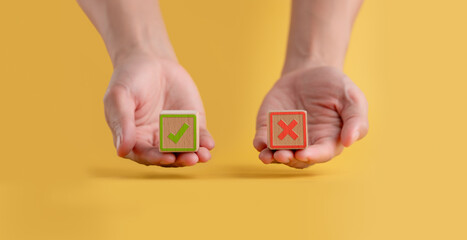 Hand holding a wooden block showing a piece of paper with symbols of right and wrong, true and false, accept and reject ,evaluation of yes or no poll votes ,opinion survey concept ,yellow background