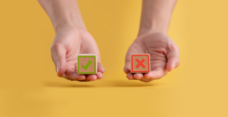 Hand holding a wooden block showing a piece of paper with symbols of right and wrong, true and...