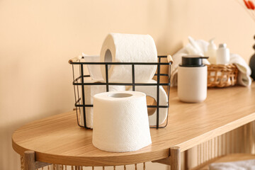 Basket with toilet paper rolls and bottle of soap on wooden table near  color wall, closeup