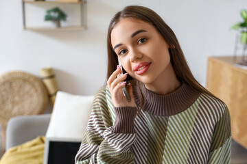 Young woman talking by mobile phone at home