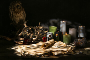 Witch's magic attributes with book, owl, crystal ball of fortune teller and candles on dark table